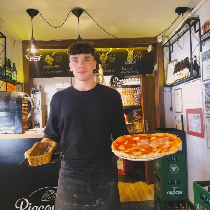 Stażysta niesie pizze i sztućce do stolika