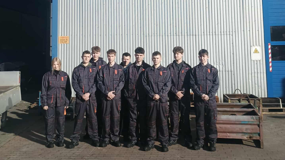 Uczniowe w strojach roboczych przed budynkiem firmy Dachpoll