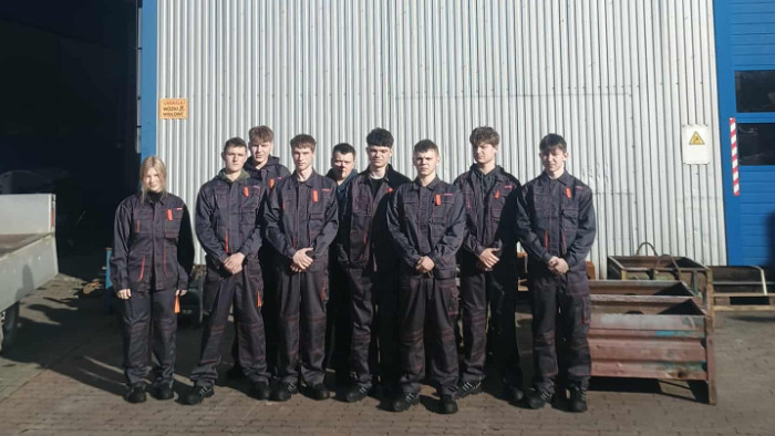 Uczniowe w strojach roboczych przed budynkiem firmy Dachpoll