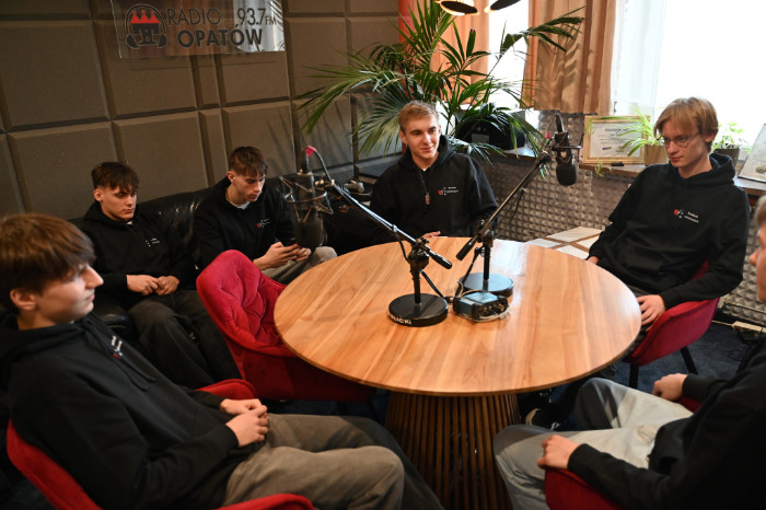 Praktykanci siedzą przy stole na który stoją mikrofony
